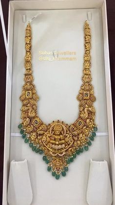 an elaborate gold necklace with green beads in a box