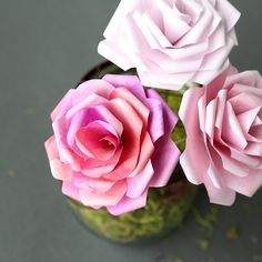 three pink and purple paper roses in a green vase on a gray surface with confetti sprinkles