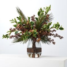 a vase filled with green and brown flowers on top of a white table next to a wall