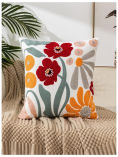 an orange and red flowered pillow sitting on top of a couch next to a plant