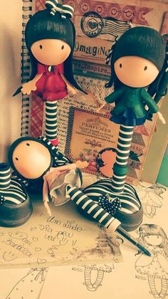 three dolls are standing next to each other on top of a table with books and papers