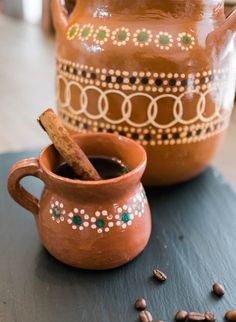 a cup of coffee with a cinnamon stick sticking out of it next to a pot