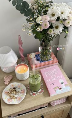 a wooden table topped with a vase filled with flowers next to a book and candle