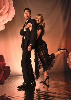 a man and woman posing for a photo in front of a backdrop with pink roses