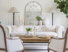 a living room filled with white furniture and lots of greenery on top of it