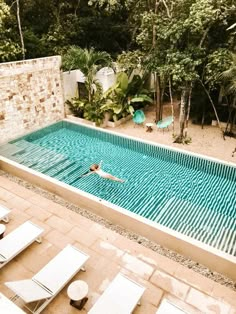 a person swimming in a pool surrounded by trees and lawn chairs with no people around it