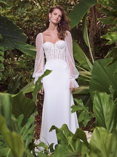 a woman in a white dress is standing among green plants and trees with her hands on her hips