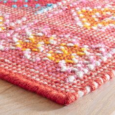 an orange and pink rug on top of a wooden floor next to a wood table