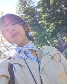 a woman wearing a white jacket and blue bow tie standing in front of some trees