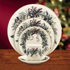 a set of christmas dinnerware with holly wreaths on the front and sides, sitting on a wooden table