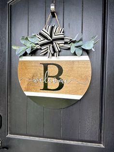 a welcome sign hanging on the front door with leaves and ribbon tied to it's side