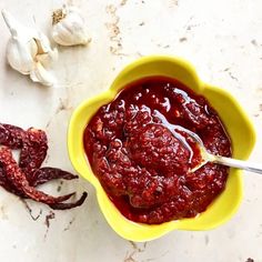 a yellow bowl filled with red sauce next to garlic