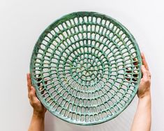 two hands holding up a green plate with holes in it on a white wall background