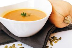 a white bowl filled with soup next to pumpkins on a cloth and black napkin