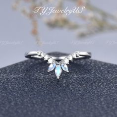 a white gold ring with blue and clear stones on it's side, sitting on top of a rock