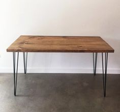 a wooden table with black hairpinks on it and a white wall in the background