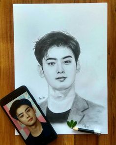 a pencil drawing of a young man next to a cell phone on a wooden table