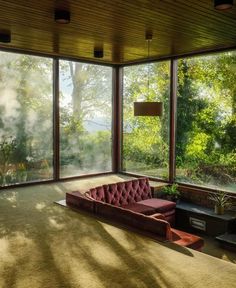 a living room filled with furniture and lots of glass doors leading out to the woods