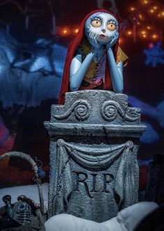 a creepy statue sitting on top of a tombstone with a red cape over it's head