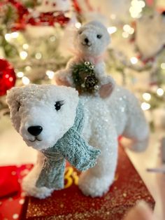 two white teddy bears sitting on top of a red box in front of a christmas tree