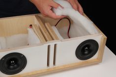 a person is cleaning the inside of a wooden box with foam and a pair of black speakers