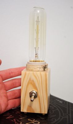 a hand holding a light bulb on top of a wooden block with a metal base