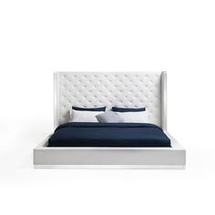 a white bed with blue sheets and pillows on it's headboard, in front of a white wall