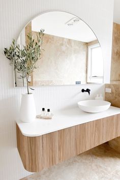 a white sink sitting under a mirror next to a vase with an olive tree in it