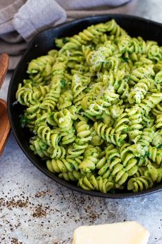 a skillet filled with pasta and pesto sauce next to a wooden spatula