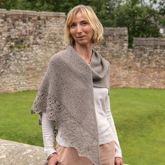 a woman standing on top of a stone wall wearing a shawl over her shoulders