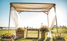 an outdoor wedding setup with flowers in wooden planters and white drapes over the top