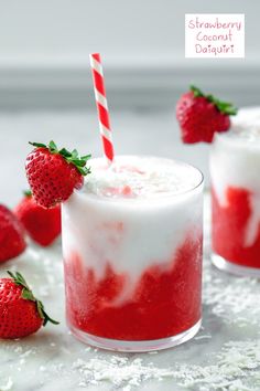 two glasses filled with strawberries and coconut drink on top of a white tablecloth