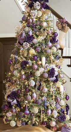 a decorated christmas tree with purple and gold ornaments on the top, in front of a stair case