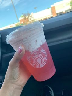 a woman holding up a cup of starbucks drink in her hand while sitting in the car