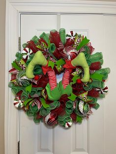 a christmas wreath with candy canes and stockings hanging from the front door, on a white door