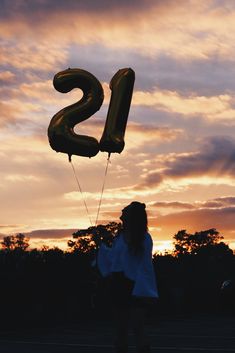 a woman flying a large black number twenty two balloon in the sky at sunset or dawn