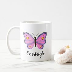 a white coffee mug with a pink butterfly on it and a donut next to it