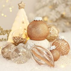 christmas ornaments are arranged in front of a white and gold tree with snow on the ground