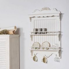 a white shelf with plates and cups on it next to a cabinet in a room