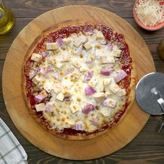 a pizza sitting on top of a wooden cutting board next to cheese and other toppings