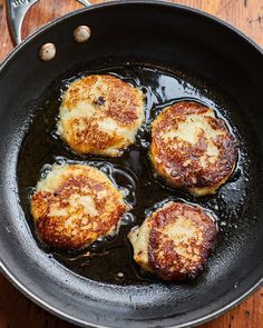 three pieces of food cooking in a skillet on top of a wooden table with utensils