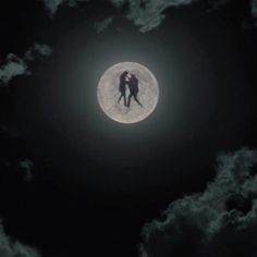 two people are standing on the moon in the dark night sky with clouds around them