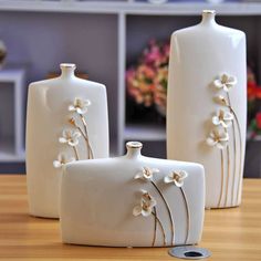 three white vases sitting on top of a wooden table next to each other with flowers painted on them