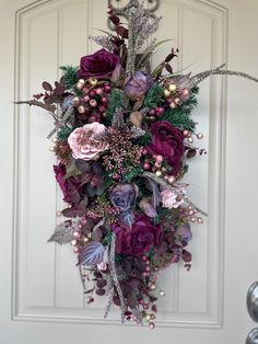 a wreath hanging on the front door decorated with purple flowers and greenery for christmas