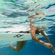 a woman is swimming in the water with her surfboard under her arm and feet