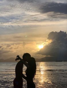 two people are kissing on the beach at sunset