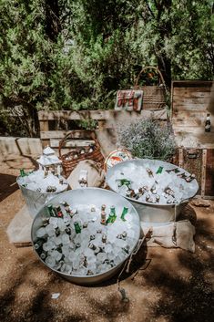 two buckets filled with ice sitting on top of a dirt ground next to trees