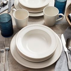 the table is set with white dishes and silverware, along with blue glass cups