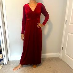 a woman standing in front of a white wall wearing a red velvet dress with long sleeves