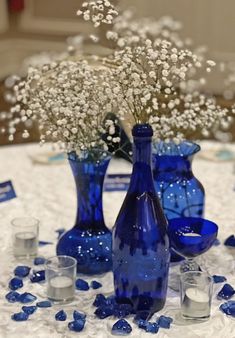 blue vases with baby's breath in them are on a white tablecloth